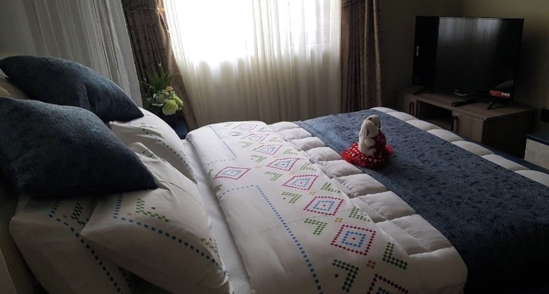 A hotel room with a bed, pillows, a blanket, a television, and a small table.