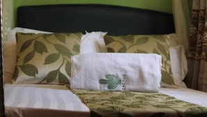 A bed with a green leaf-patterned pillow, a white pillow with a cactus logo, and a white blanket. - Cactus Hill Side Hotel (Gulu)