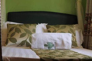 Un lit avec un oreiller à motifs de feuilles vertes, un oreiller blanc orné du logo d’un cactus et une couverture blanche.