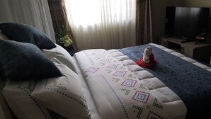 A hotel room with a bed, pillows, a blanket, a teddy bear, a television, and curtains. - Cactus Hill Side Hotel (Gulu)