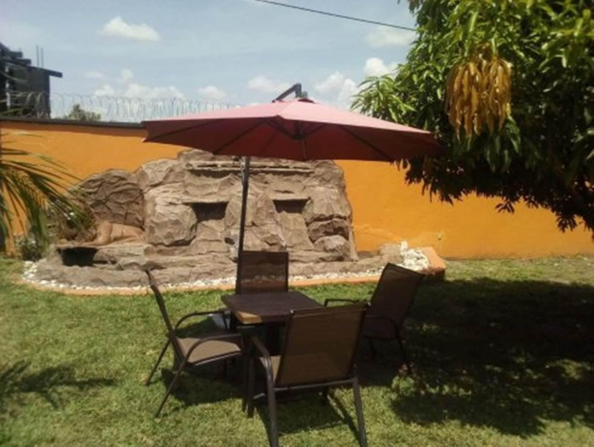 An outdoor patio with a table and chairs, a red umbrella, and a rock wall with a small pond.