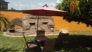 An outdoor patio with a table and chairs, a red umbrella, and a rock wall with a small pond.
