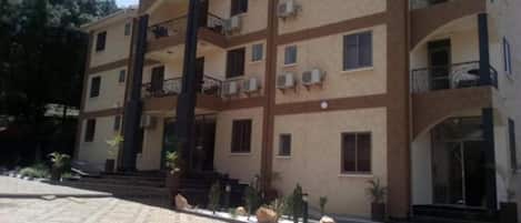 A multi-story building with balconies, air conditioning units, and a paved entrance area.