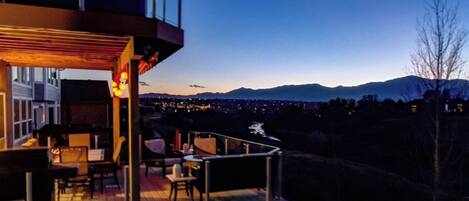 A modern outdoor deck with seating and a view of a cityscape and mountains.