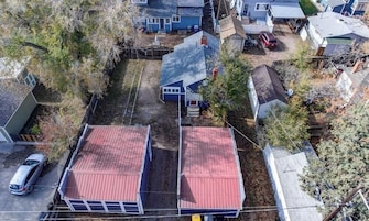 A residential area with two houses, one with a red roof and another with a grey roof, surrounded by trees and a parked car.