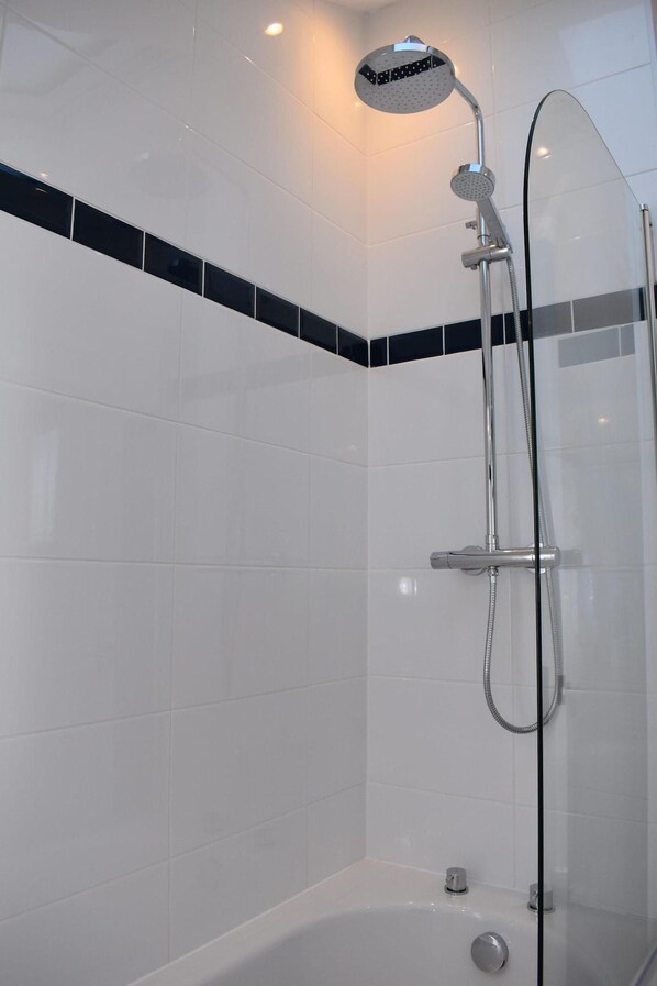 Ducha moderna con cabezal de ducha de mano y bañera con mampara de vidrio.