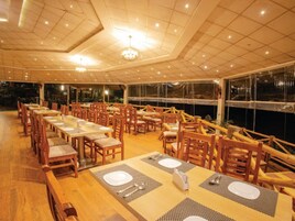 Un restaurante con mesas y sillas de madera, techo de baldosas y grandes ventanales.