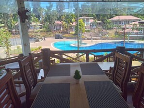Un espacio al aire libre con mesas y sillas, con vista a una piscina y edificios circundantes.