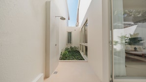 Un pasillo estrecho con ducha, un pequeño jardín y una puerta de cristal corredera que da a un balcón.