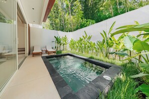 Ein moderner Poolbereich im Freien mit freiem Blick zum Himmel, umgeben von üppiger Vegetation und einer weißen Mauer.