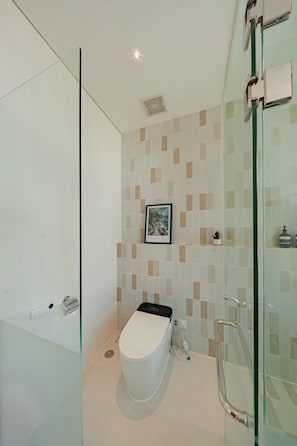A modern bathroom with a glass shower enclosure, a toilet, and a small shelf with toiletries. - Villa Binginzie by Betterplace (Bingin)