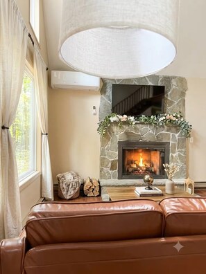A cozy living room with a stone fireplace, leather sofa, and a large lamp. - Sauna Retreat 3-bedroom 3 bathroom Chalet House with AC (Tobyhanna)