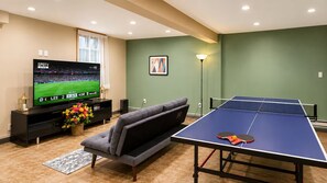 A living room with a flat-screen TV, a sofa, a table tennis table, and a flower arrangement. - Sauna Retreat 3-bedroom 3 bathroom Chalet House with AC (Tobyhanna)