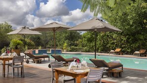 A poolside area with lounge chairs, umbrellas, and a dining table set for two. - Sedia Riverside Hotel (Maun)