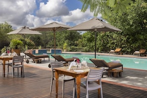 A poolside area with lounge chairs, umbrellas, and a dining table set for two. - Sedia Riverside Hotel (Maun)
