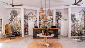 A lobby with a round table, wicker chairs, a reception desk, and a ceiling fan. - Sedia Riverside Hotel (Maun)