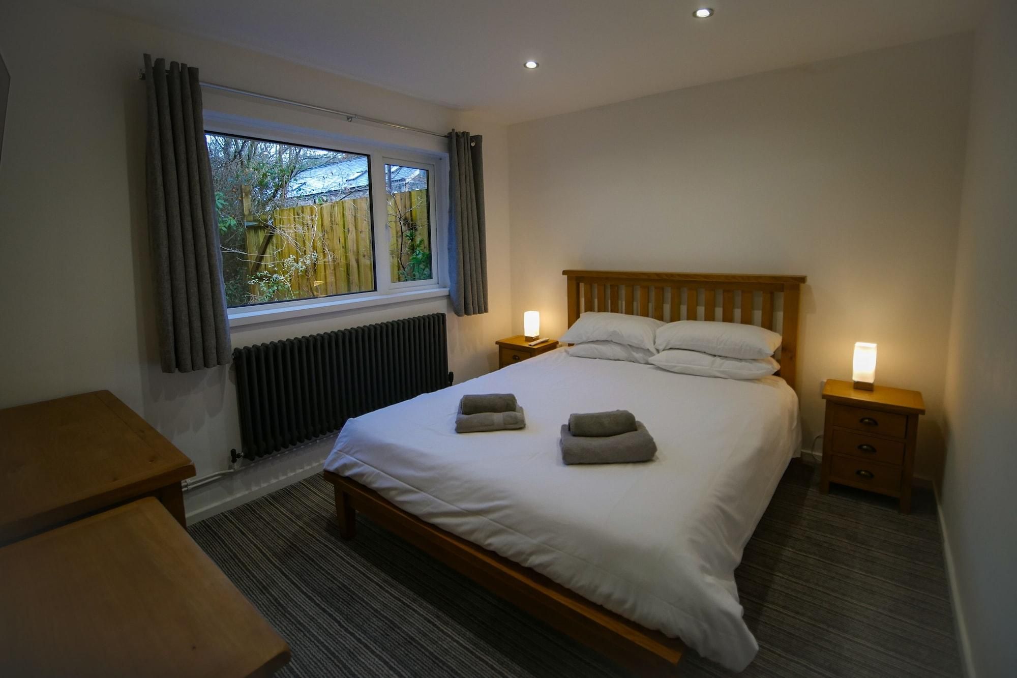 A bedroom with a large bed, two bedside tables with lamps, a window with curtains, and a radiator.