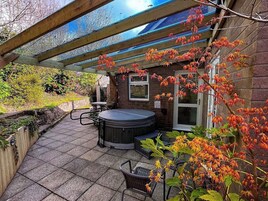 Un patio con jacuzzi, mobiliario exterior y una pérgola cubierta de plantas trepadoras.