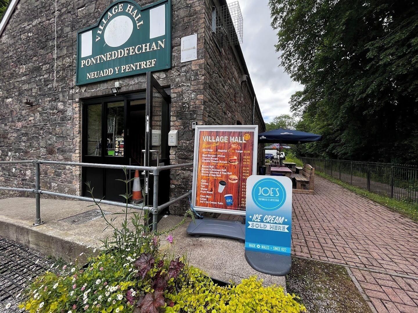 A stone building with a sign for Village Hall and a menu board.