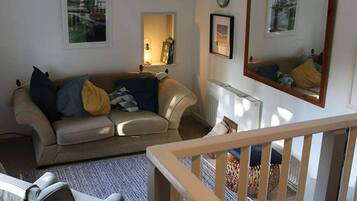 A living room with a sofa, a coffee table, and a chair. There is a window with a view of boats, a lamp, and a framed picture on the wall.