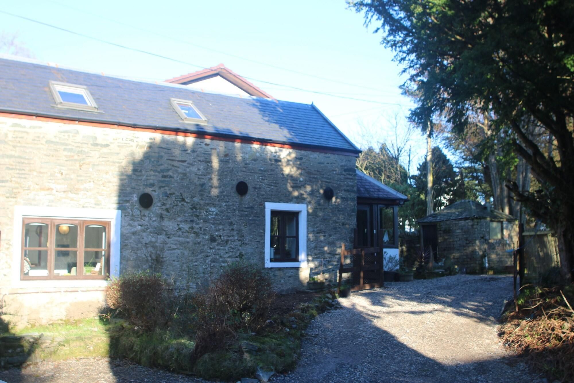 A stone building with a sloped roof, a gravel driveway, and a small wooden structure to the right.