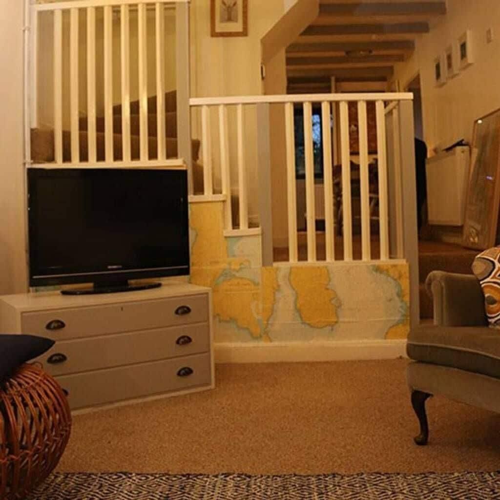 Ein Wohnzimmer mit Fernseher, einem weißen Schrank, einem Korbstuhl, einem gemusterten Teppich und einem weißen Geländer mit einer Karte.