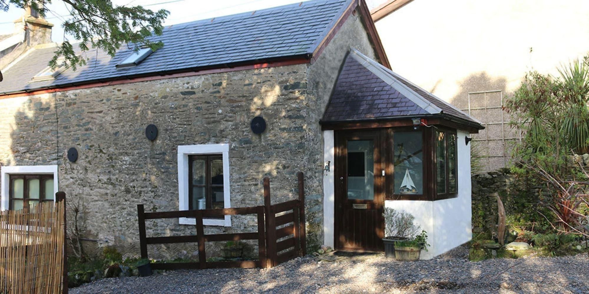 A stone house with a wooden gate, a small porch, and a window with a sailboat decoration.