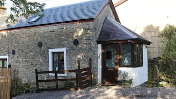 A stone house with a wooden gate, a small porch, and a window with a sailboat decoration.