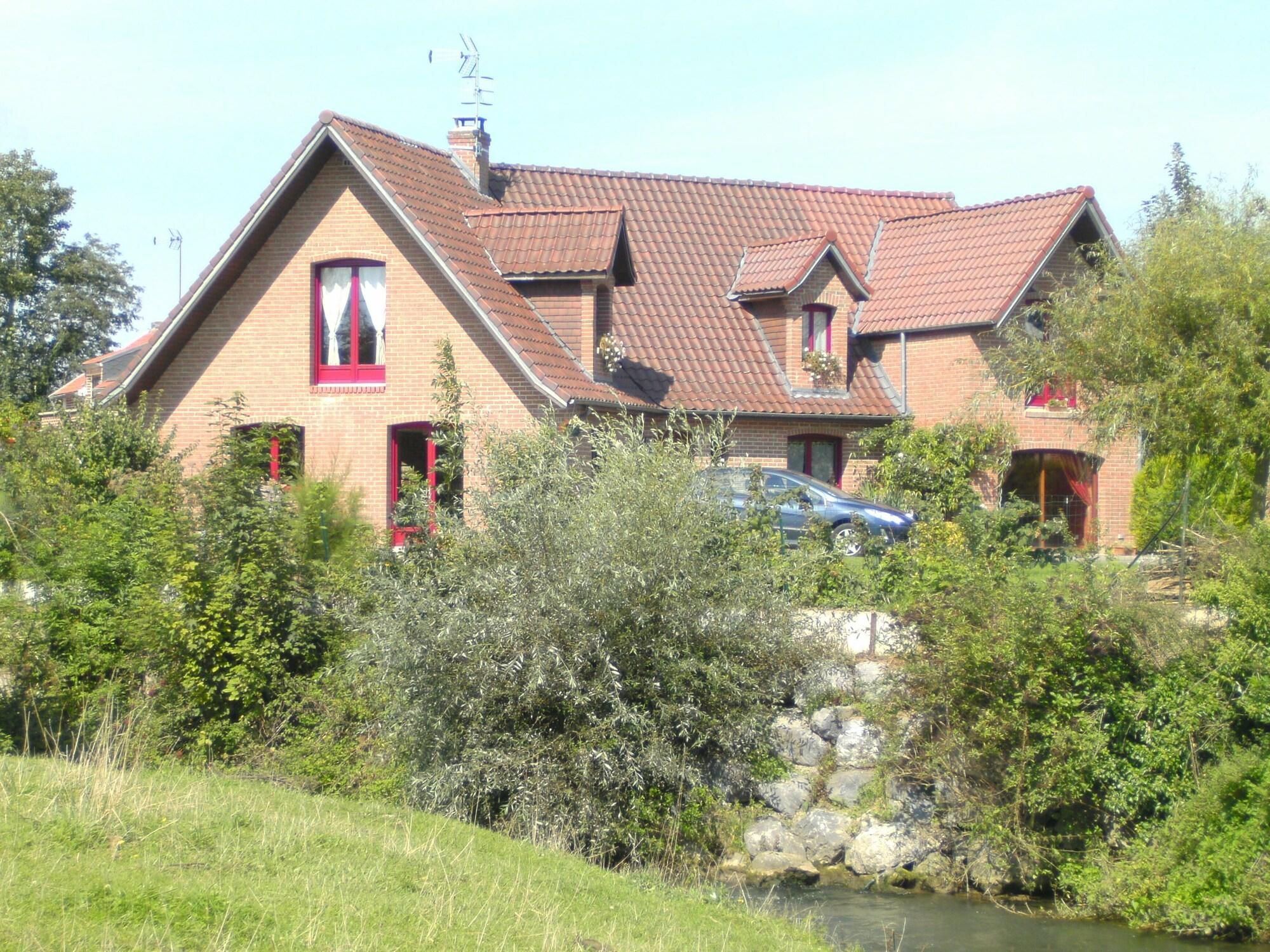 A two-story house with a red-tiled roof, a chimney, and a small garden area with a pond.