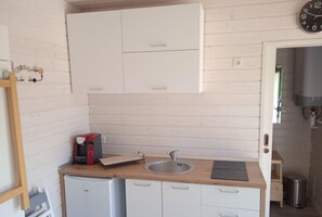 Una cocina compacta con armarios blancos, un lavamanos de acero inoxidable y una cafetera.