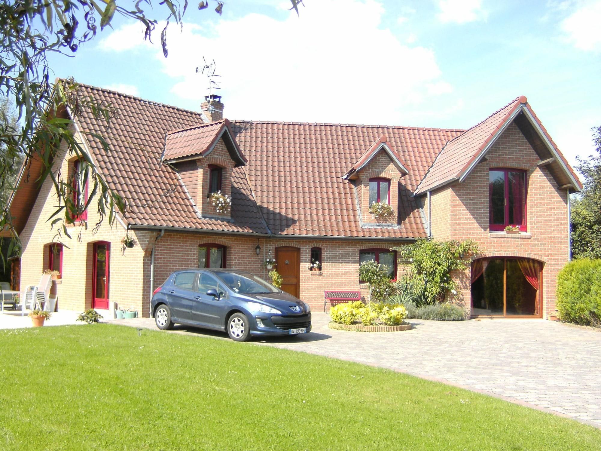 Uma casa de dois andares com um carro na entrada, um gramado bem cuidado e fachada de tijolos.