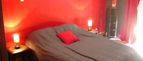 A bedroom with a large bed, red walls, and a nightstand with a lamp.