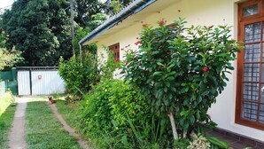 Uma trilha leva a um edifício com fachada branca e janela com padrão quadriculado.