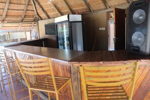 A bar area with a counter, stools, and a refrigerator. - Wingate Hotel Maun (Francistown)