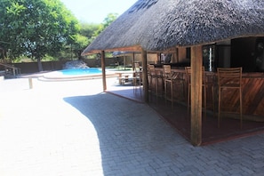 A covered outdoor seating area with a pool in the background. - Wingate Hotel Maun (Francistown)