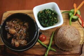 A meal with a stew, a bowl of greens, and a round bread on a wooden board. - Wingate Hotel Maun (Francistown)