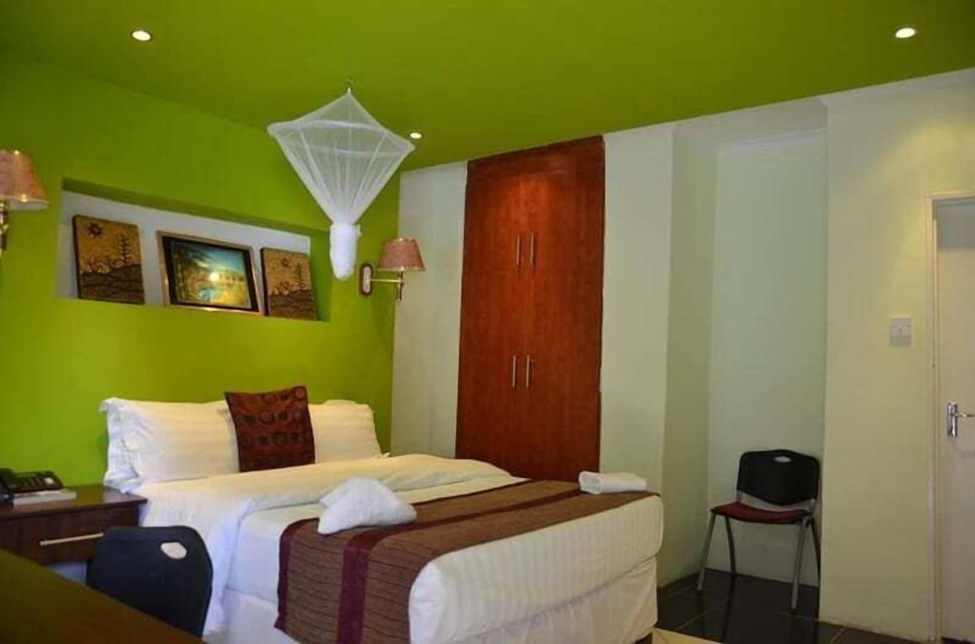 A hotel room with a bed, a chair, a wardrobe, and artwork on the wall.
