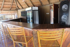 A bar area with wooden chairs, a counter, and a refrigerator. - Wingate Hotel Maun (Francistown)