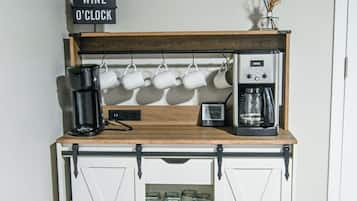 Une petite cuisine équipée d’une machine à café, d’un panneau indiquant « l’heure de l’apéro » et d’une horloge murale.