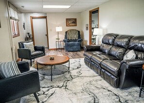 A living room with a leather sofa, a striped armchair, a round coffee table, and a blue armchair.