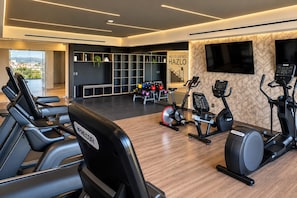 A modern gym with exercise equipment, a wall-mounted TV, and a view of the outdoors. - Chic Versalles Condo • Infinity Pool, Coworking (Puerto Vallarta)