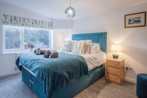 A bedroom with a bed, a bedside table, a lamp, a window with curtains, and a picture on the wall.