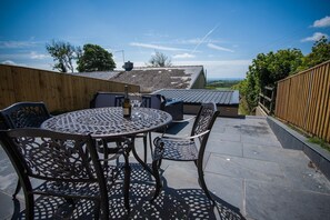 An outdoor patio with a round table and chairs, a bottle of champagne, and a view of the countryside.