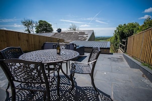 An outdoor patio with a round table and chairs, a bottle of champagne, and a view of the countryside.