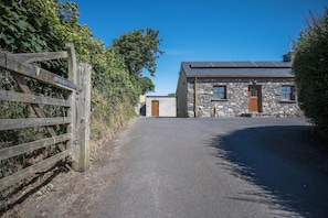 A stone building with a gravel driveway leading to a wooden gate.