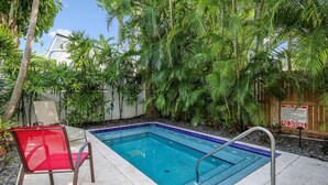 En swimmingpool med en röd stol och metallräcken, omgiven av frodig grönska och ett trästaket.