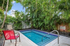 Una piscina amb una cadira vermella i baranes metàl·liques, envoltada de vegetació exuberante i una tanca de fusta.
