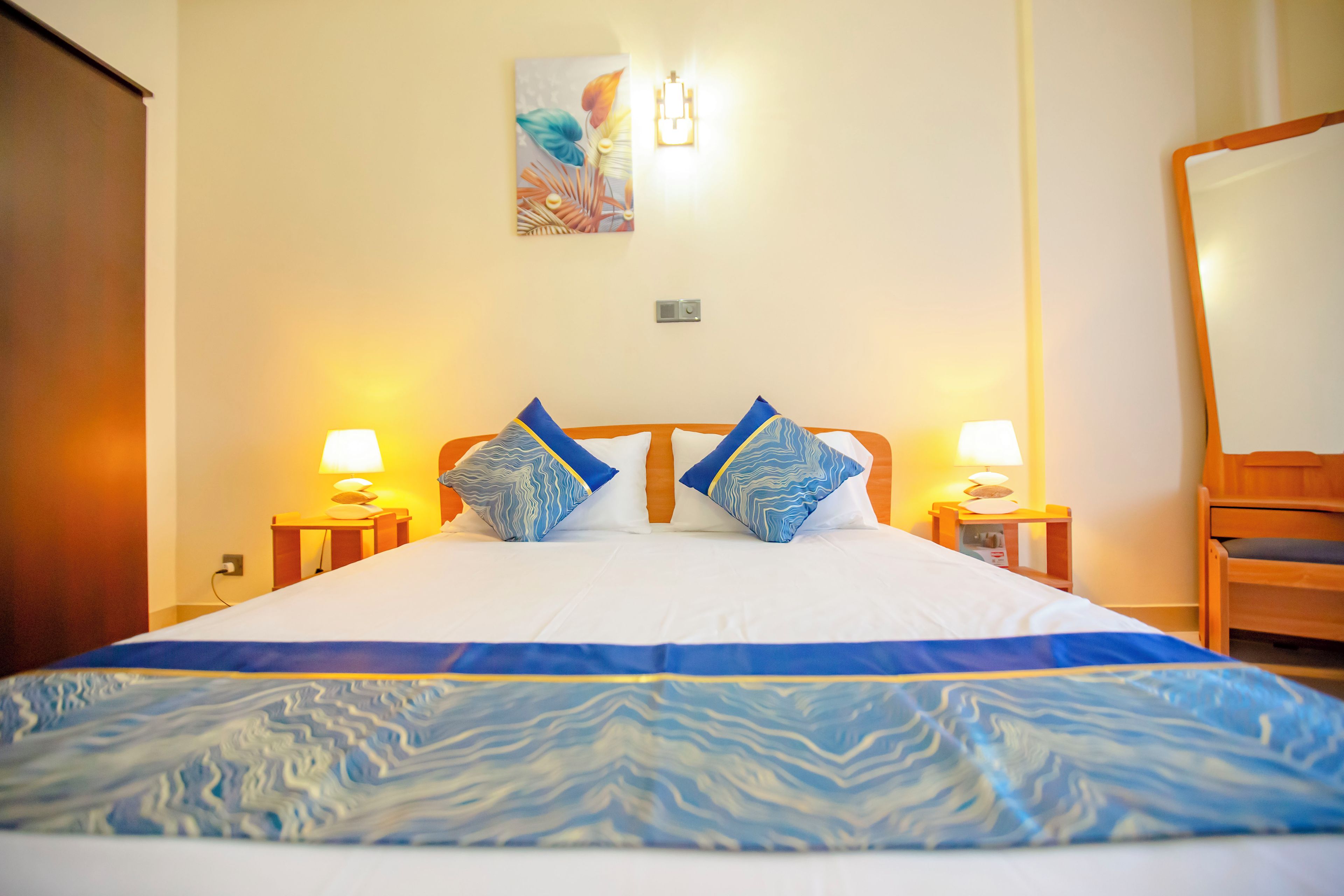 A hotel room with a large bed, two bedside lamps, a wooden chair, and a painting on the wall.