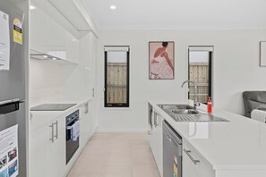 A modern kitchen with white cabinetry, stainless steel appliances, and a central island with a sink. - The Helensvale Haven | Modern 4BR Family Retreat (Helensvale)