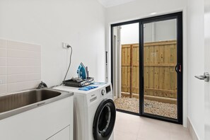 A compact laundry room with a washing machine, a sink, and a drying rack. - The Helensvale Haven | Modern 4BR Family Retreat (Helensvale)